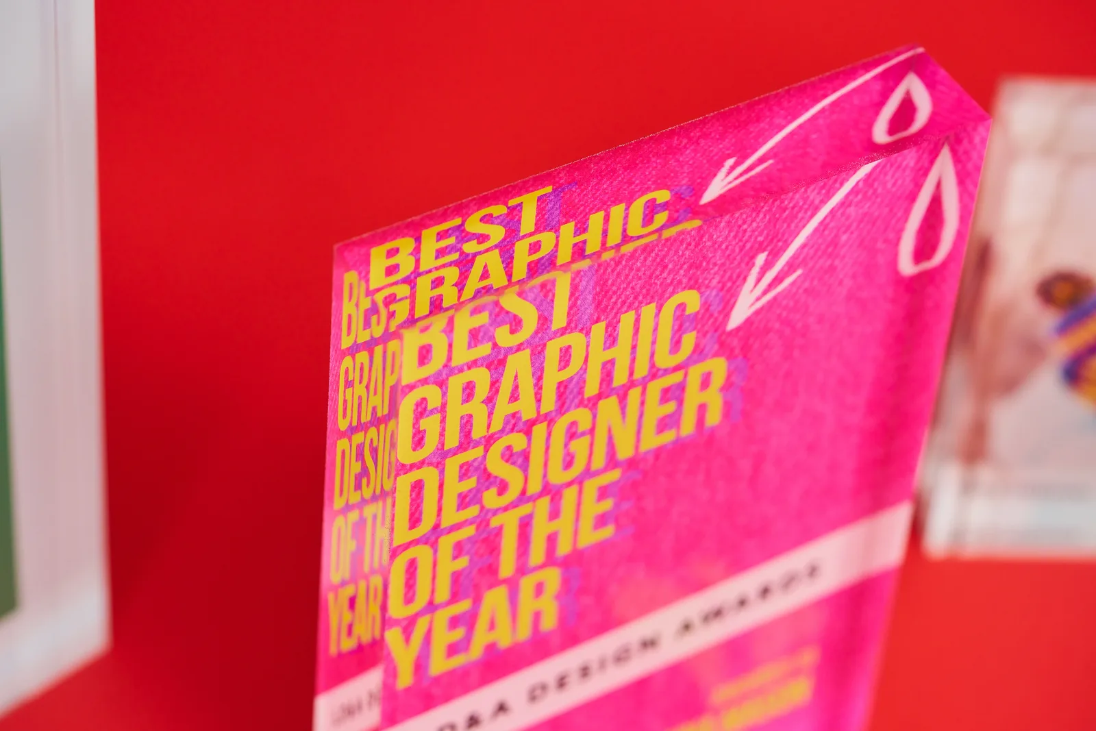 pink printed acrylic photo block with yellow text 'best graphic designer of the year' white arrow on a bright red background