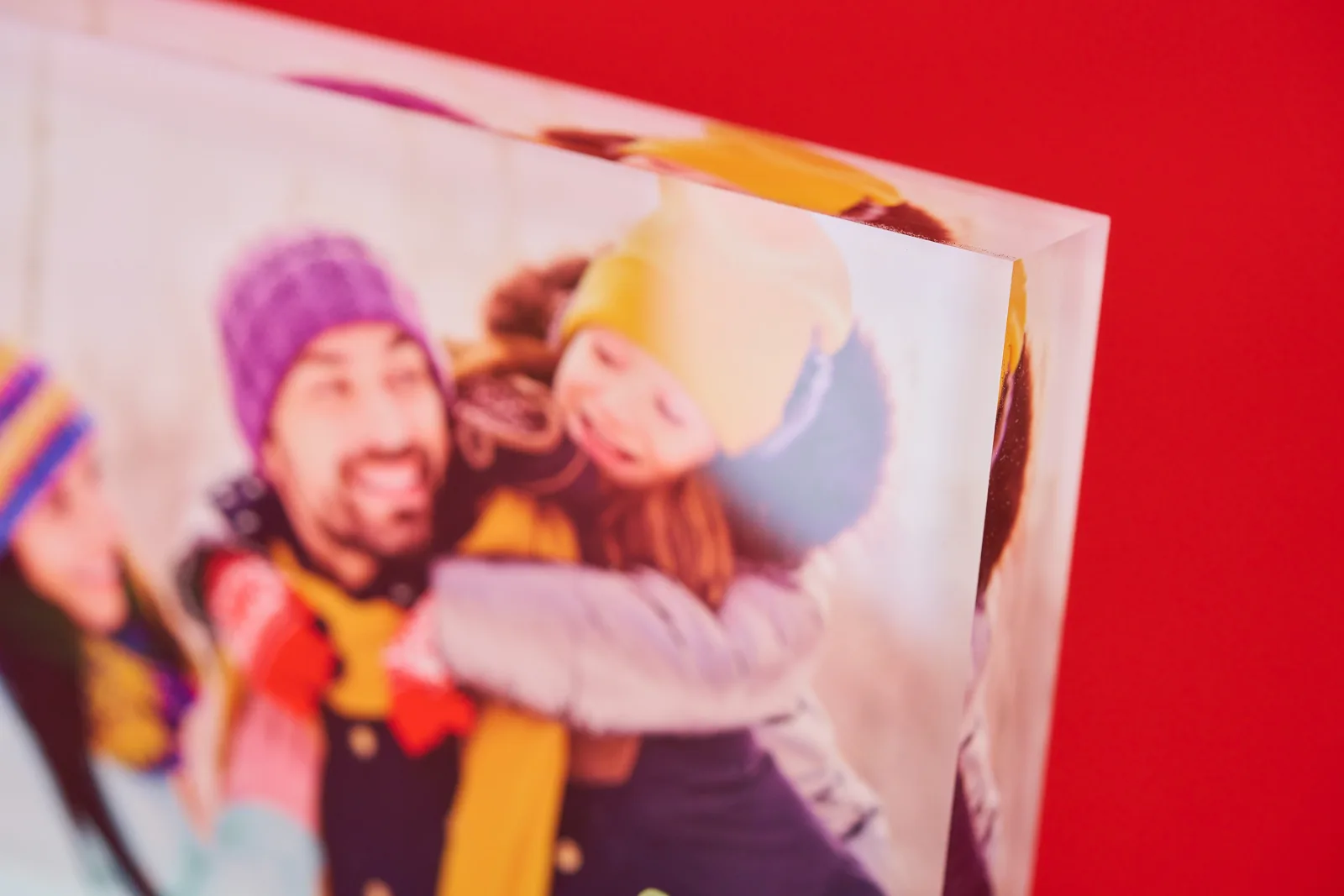 close up of a printed acrylic block with picture of a mother father and daughter playing in the snow with wooly hats and jackets on a bright red background