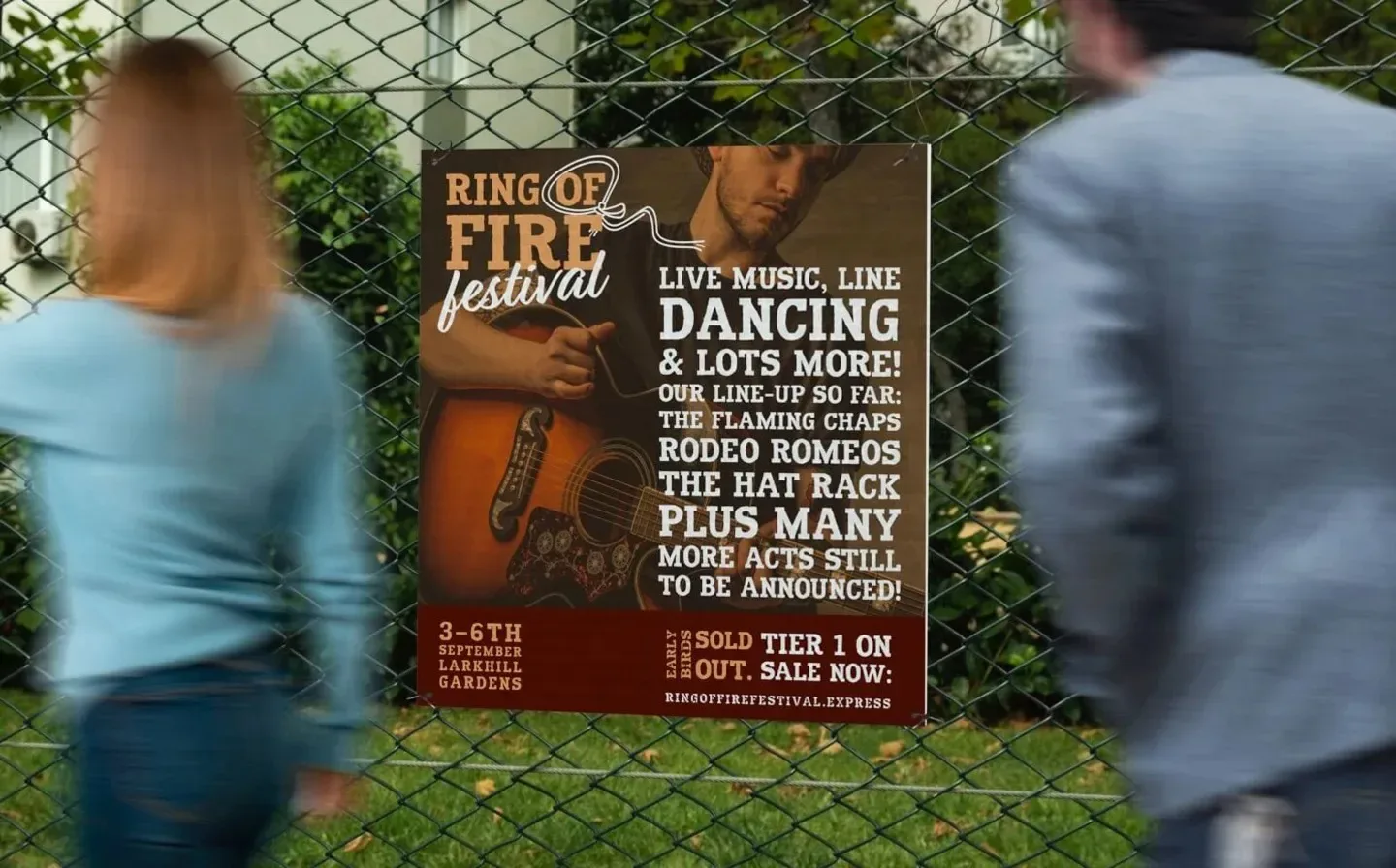 A couple strolls past a fence displaying a vibrant bubble board for a music festival