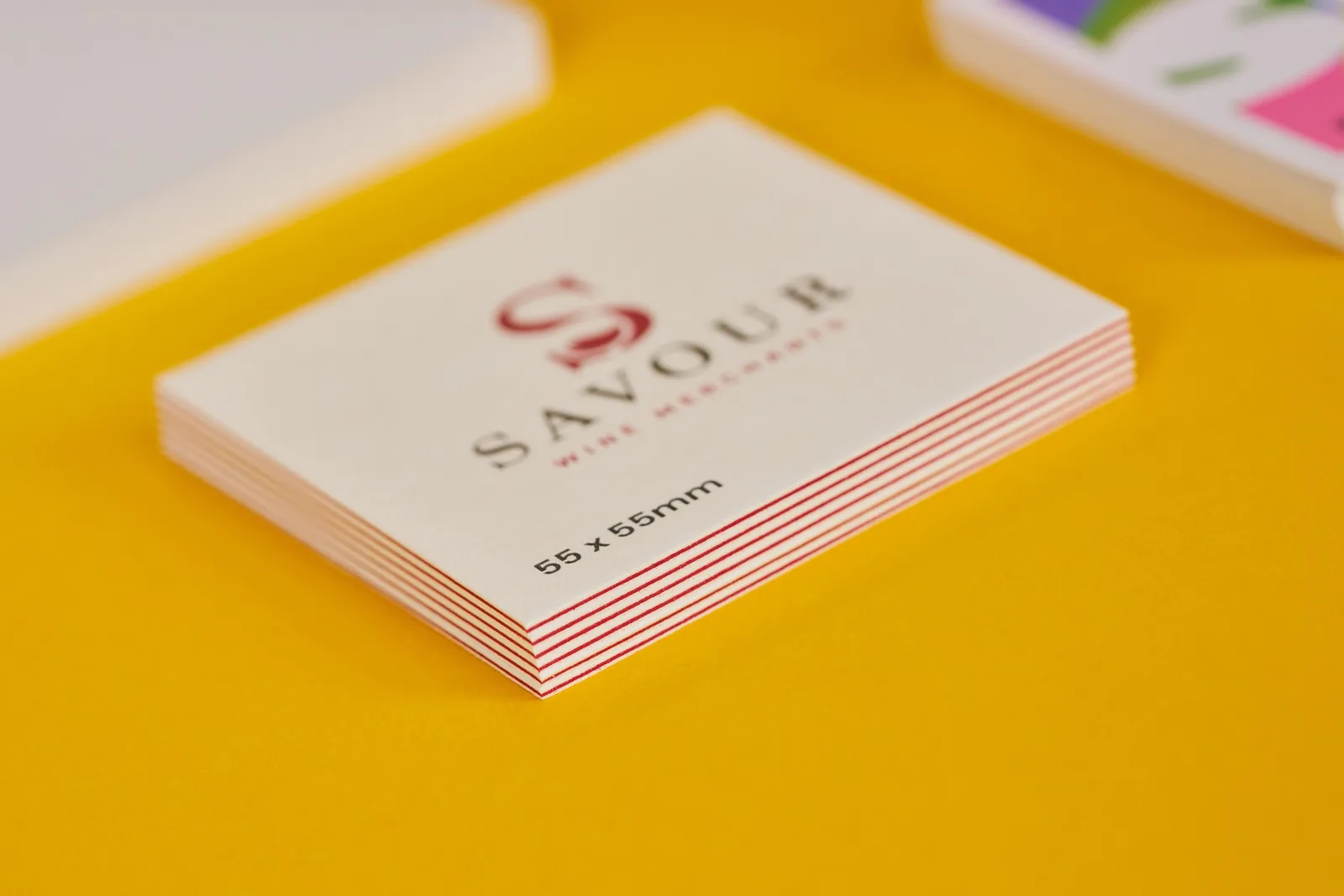 pile of square 55 x 55mm luxe printed business cards with red centre and text 'savour wine merchants' on a bright yellow background