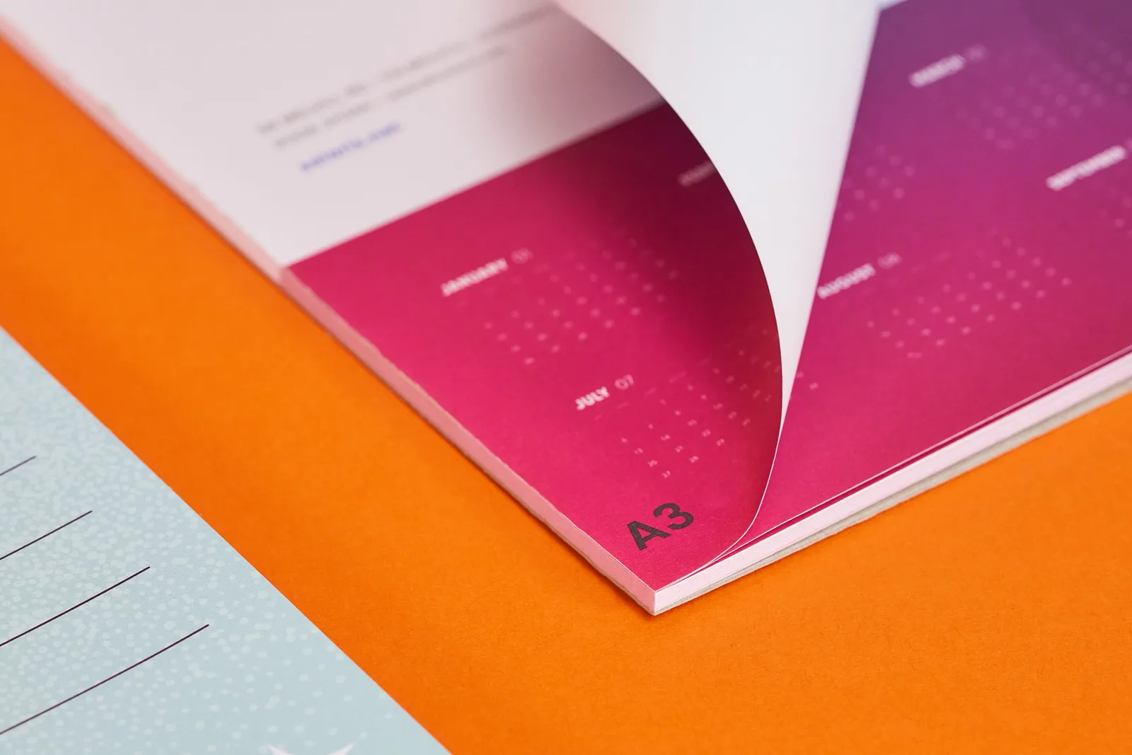 close up of an a3 purple printed desk pad with page curled over on a bright orange background