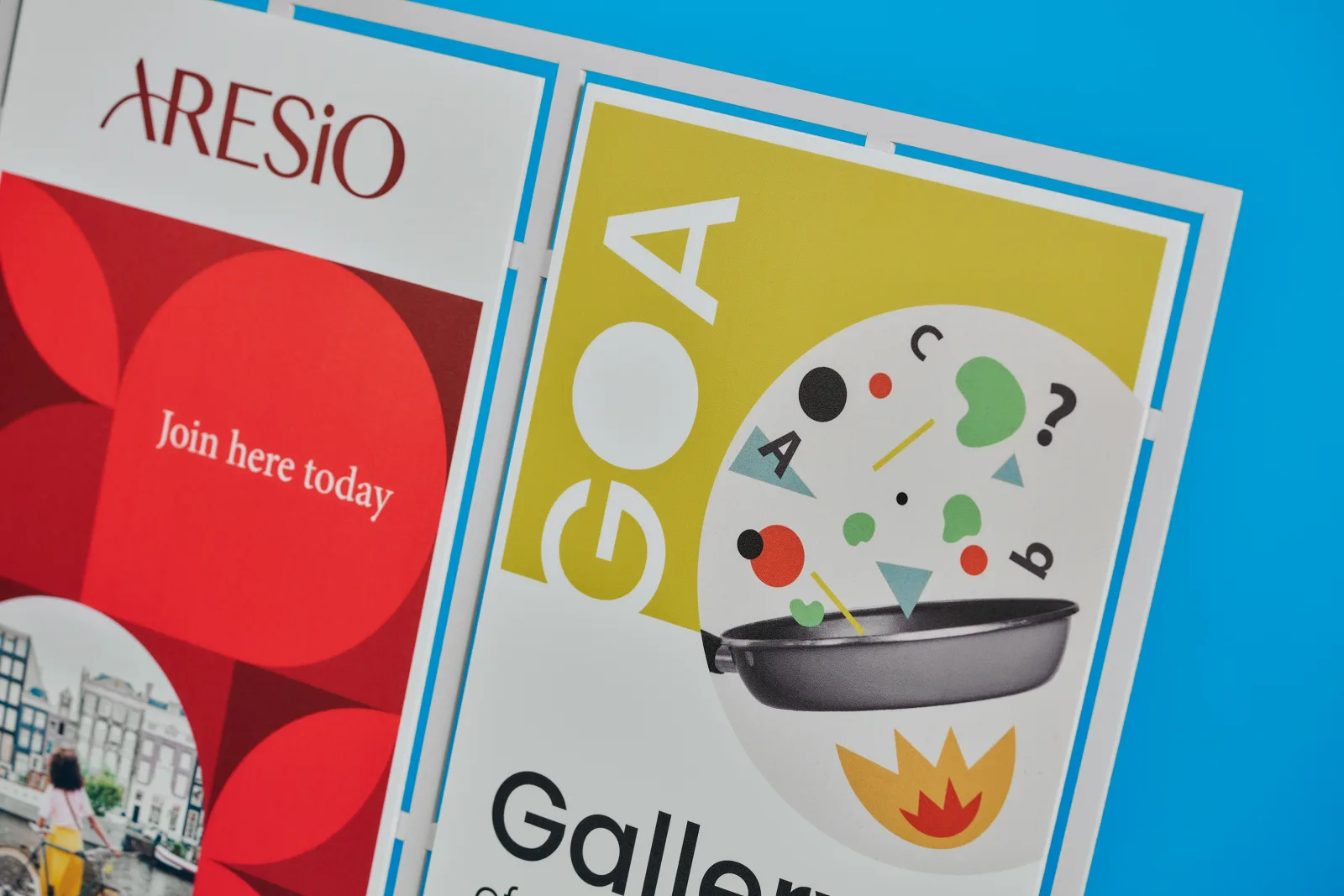 detail of 2 printed foamex exhibition graphics with text 'aresion, join here today, goa, gall' a frying pan illustration with flame, shapes and letters on a bright blue background