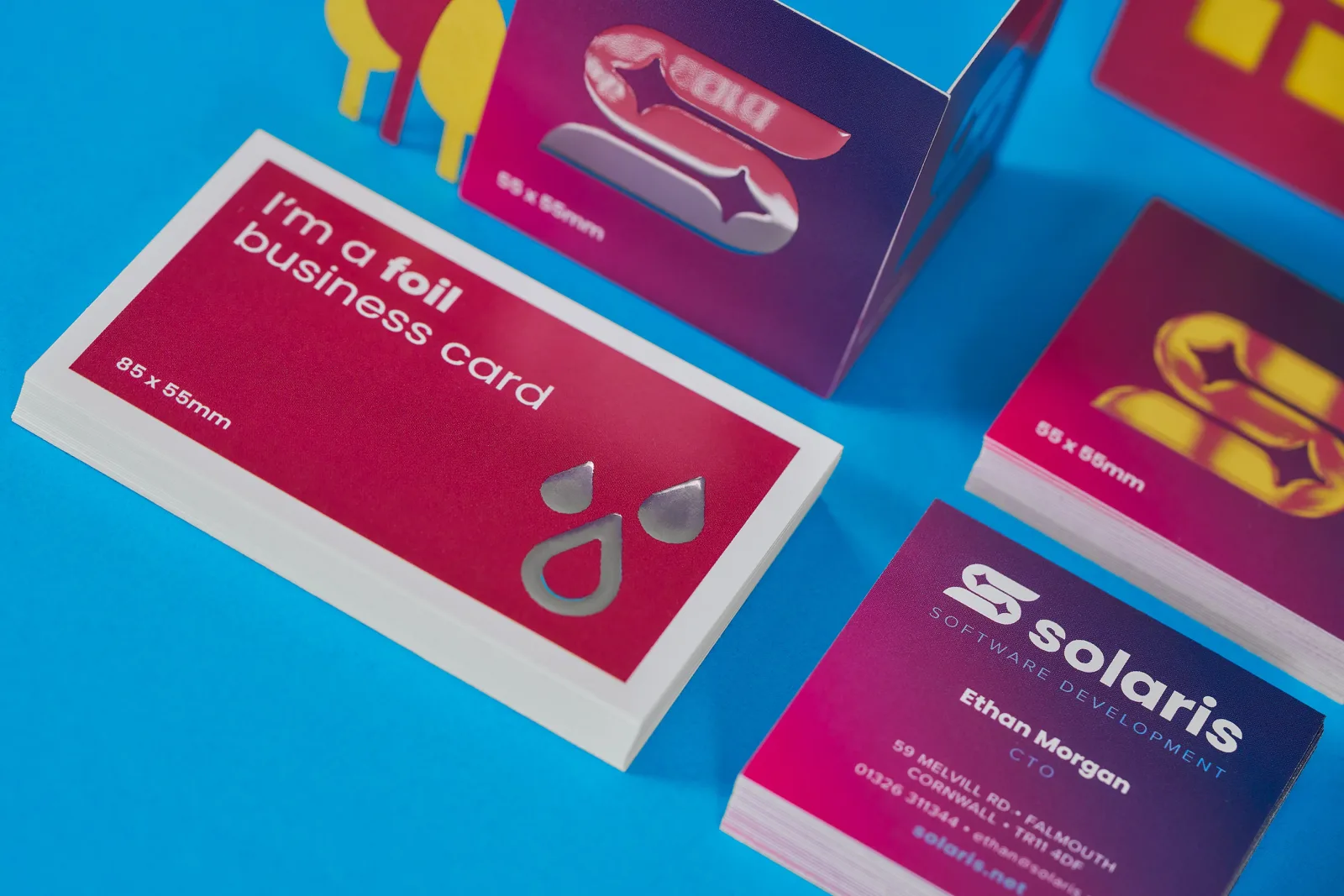 3 stacks of business cards with gold and silver foiling with text 'i'm a foil business card, solaris' on a bright blue background with purple and yellow trees