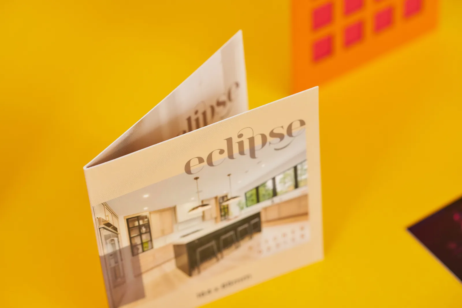 cream folded business card with text 'eclipse' on a bright yellow background with orange and red paper building