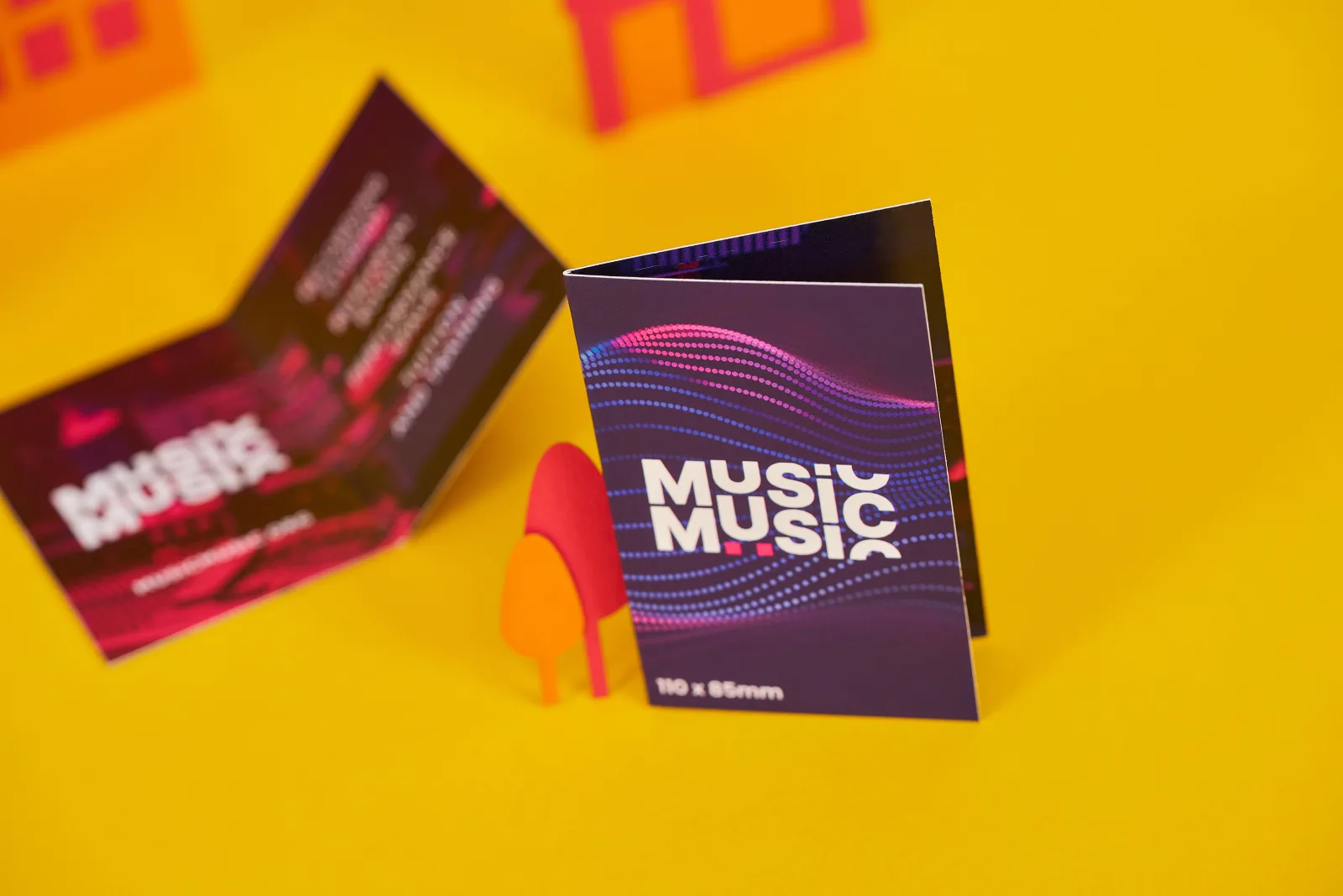 2 purple and pink printed and folded business cards with the text 'music' on a bright yellow background with red and orange paper trees