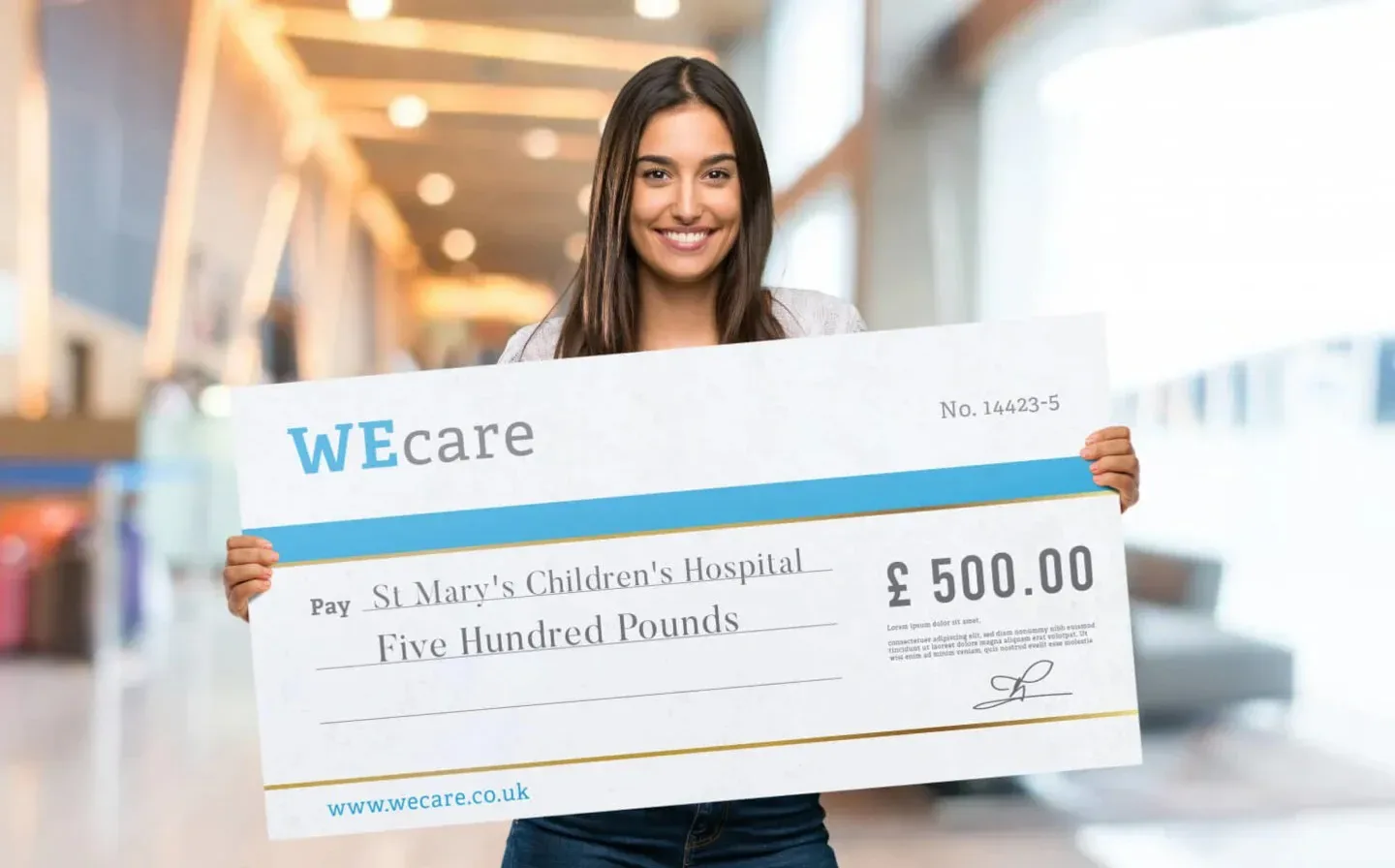 A woman proudly displays a giant check for a £500 donation, with a beaming expression of happiness