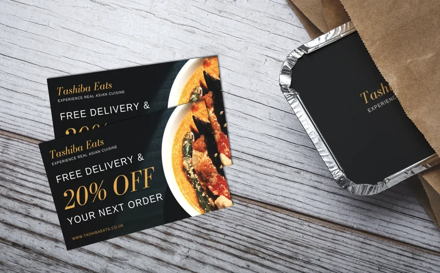 Two gift vouchers for "20% off" on a wooden table next to a paper delivery bag with takeaway food inside