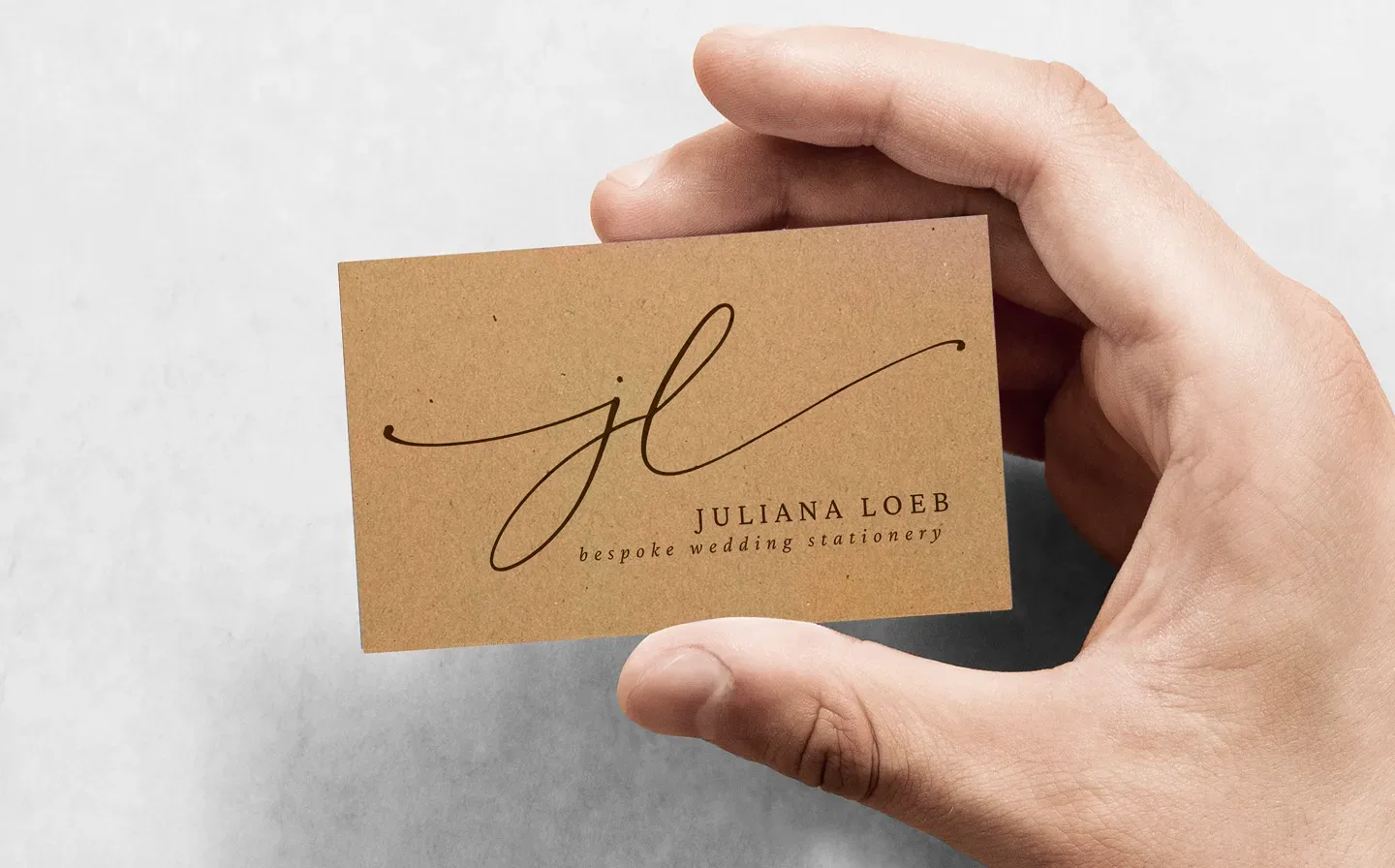 Hand holding a rustic kraft business card featuring details for a bespoke wedding stationery company