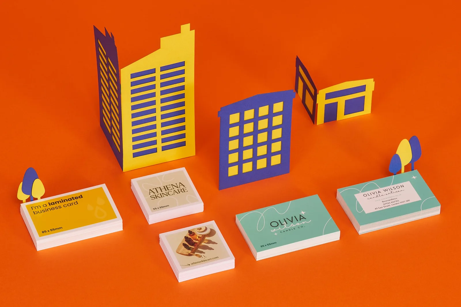 1 pile of bright yellow 85mm x 55mm business cards with wording 'i'm a laminated business card'. 2 piles of 55mm x 55mm cream business cards with wording 'athena skincare'. 2 piles of 85mm x
