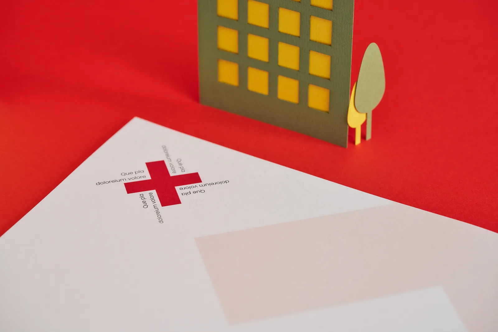 close up of a printed letterhead with a red cross and lettering on a bright red background with green and yellow paper building and trees