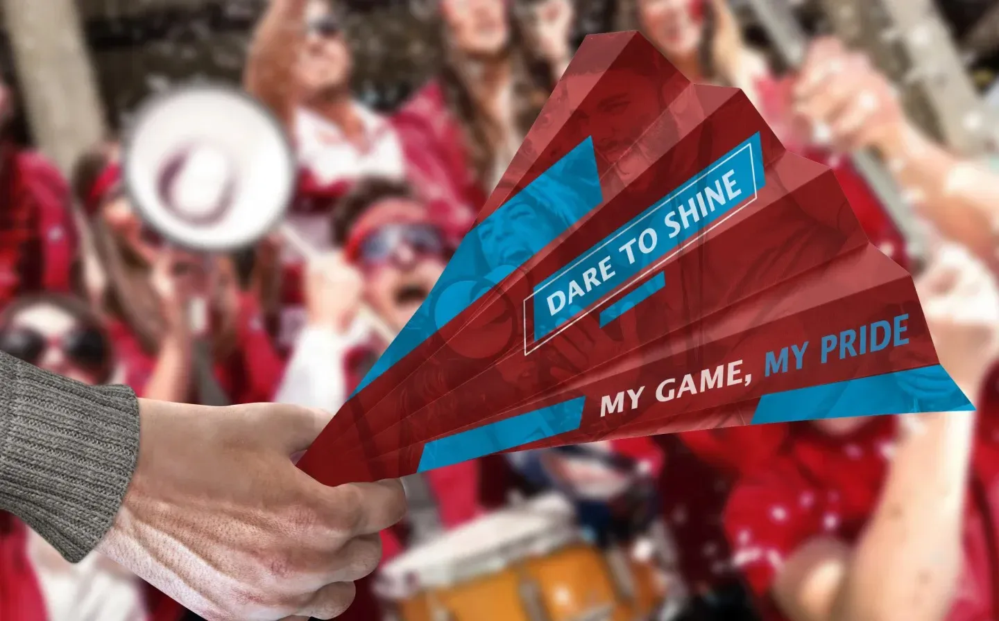 A hand grips a paper fan, embellished with a vibrant red and blue design