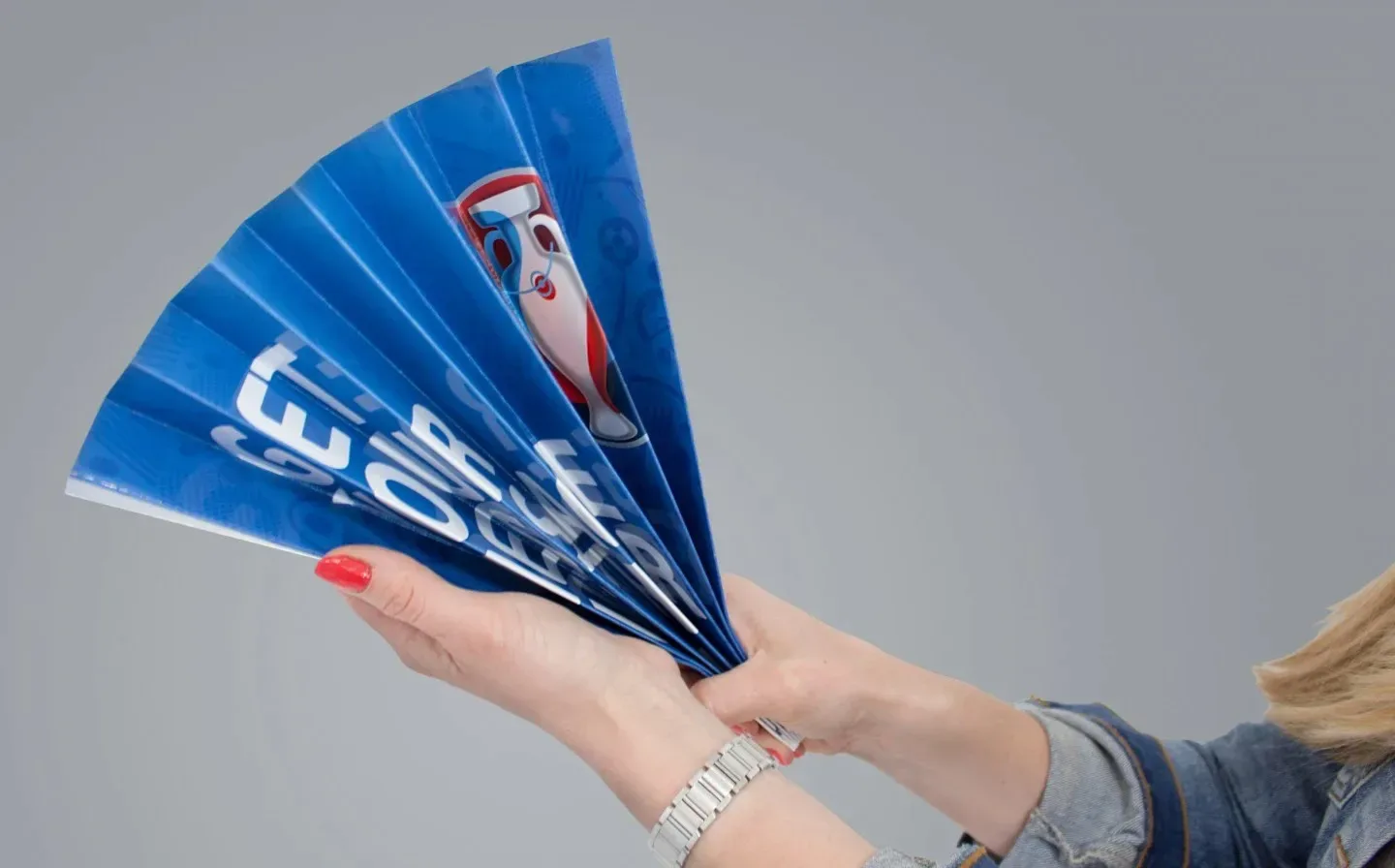 A woman elegantly displays a blue and white paper fan, showcasing its intricate design and vibrant colours