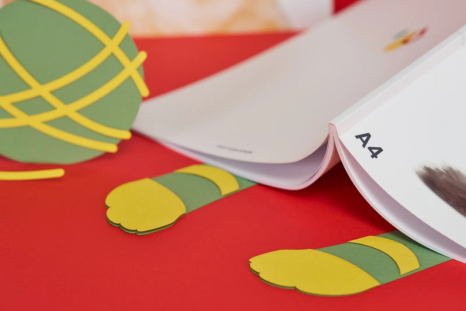 Close up of A4 perfect bound book binding with paper cat paws sticking out chasing a paper ball of wool on bright red background