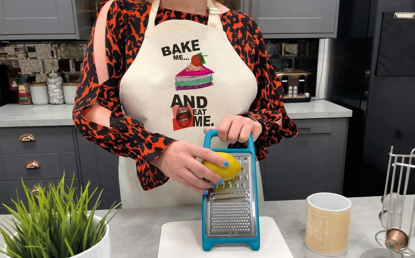 A woman in a kitchen apron grates a lemon using a grater