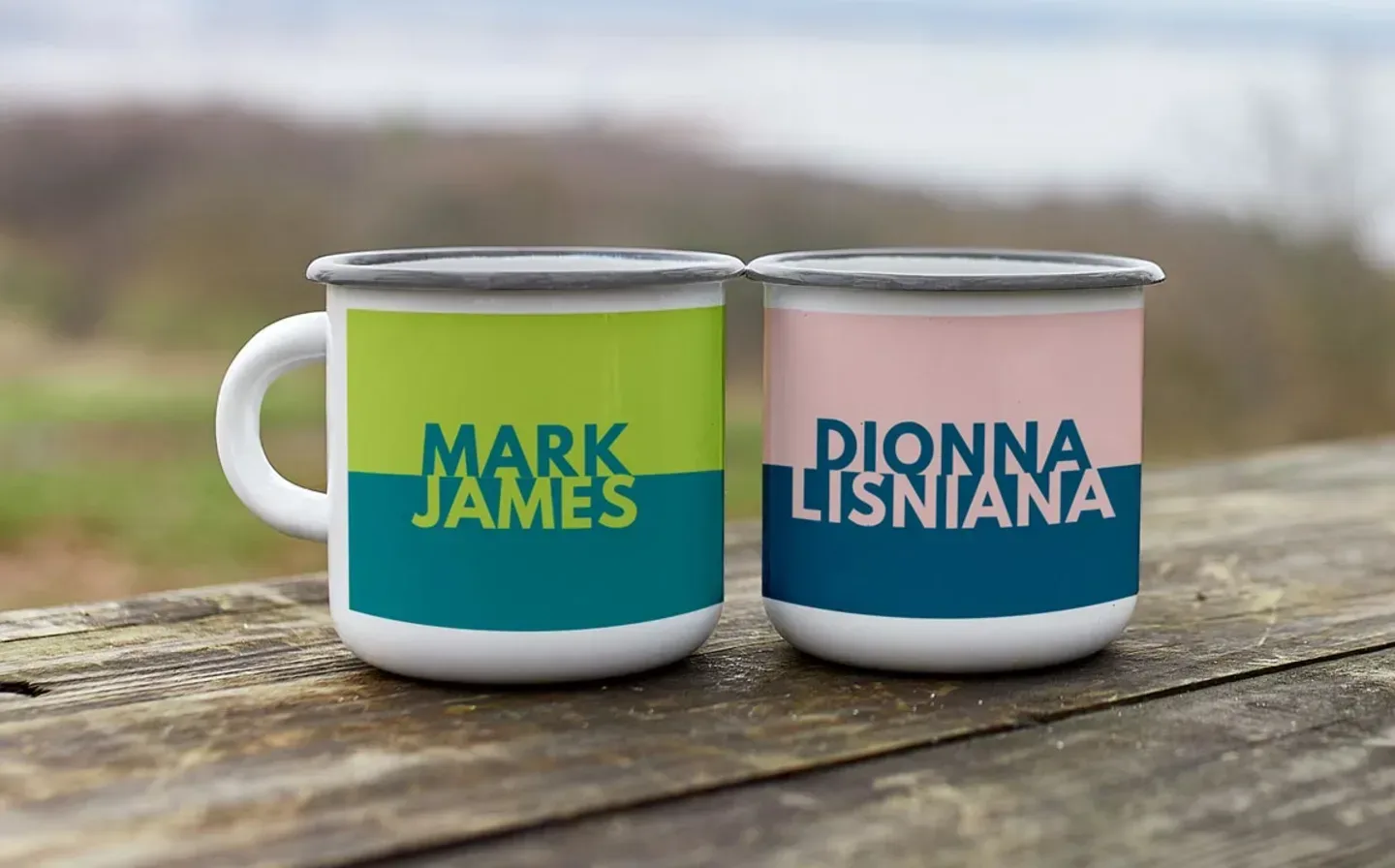 Two colourful enamel mugs featuring names, displayed side by side on a wooden table outdoors