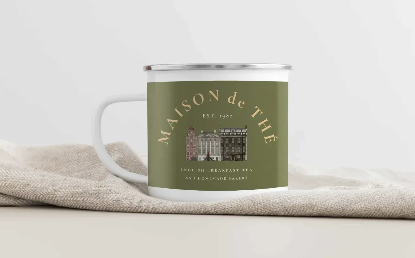 A green and white enamel mug with an elegant design, placed on a fabric surface on a plain background