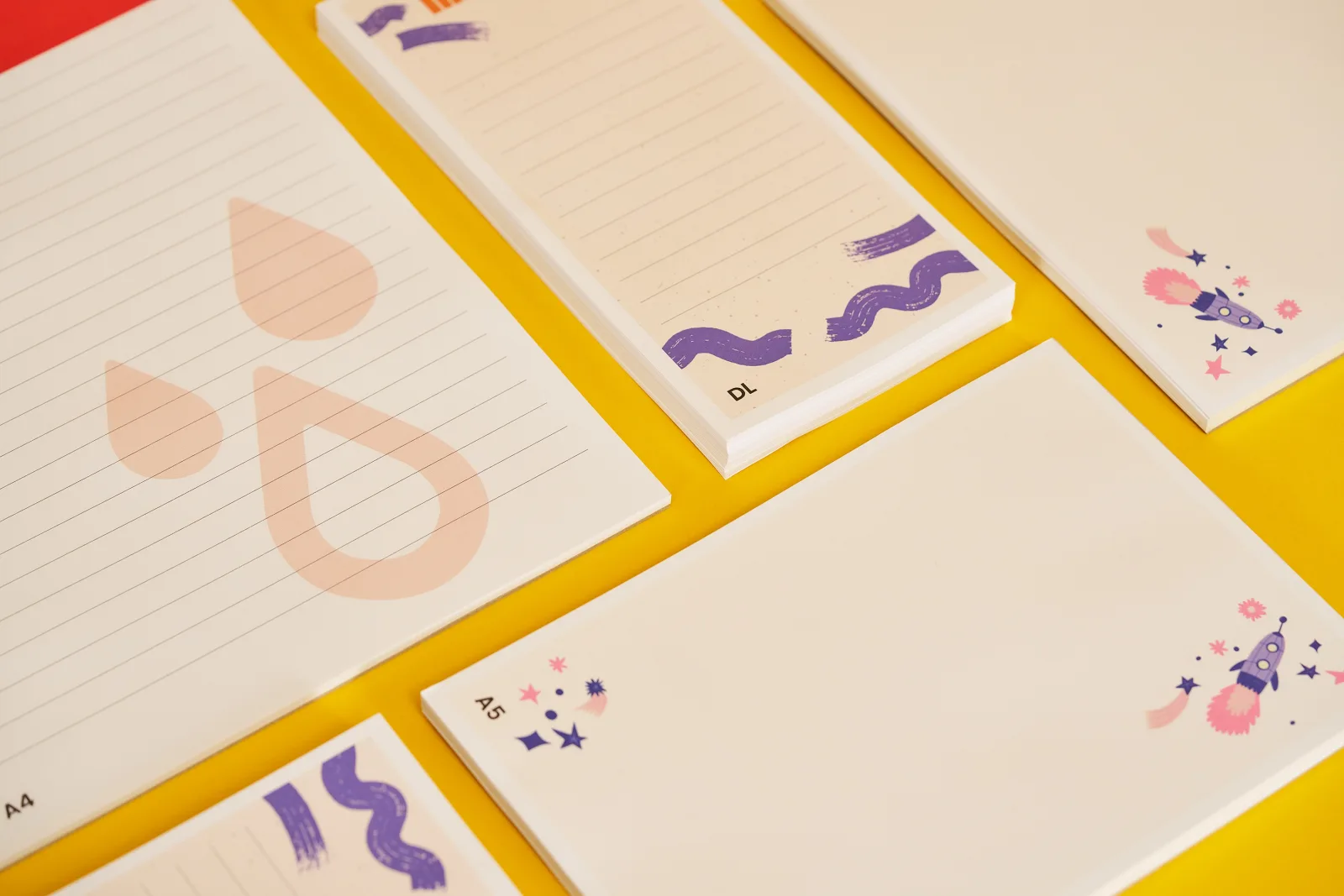 4 printed notepads dl, a5 and a4 on a yellow background with orange and red paper musical notes