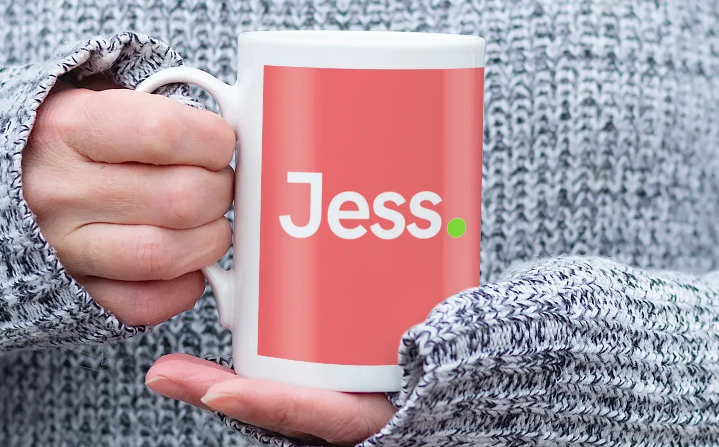 A person holding a pink porcelain mug inscribed with the name "Jess" in a stylish font