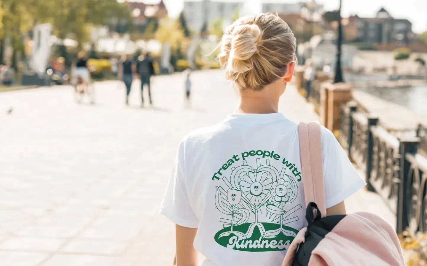 A girl wearing a white organic t-shirt that reads "treat people with kindness" carries a backpack