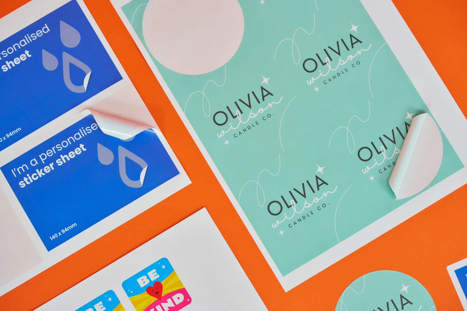 circle, rectangle and square sticker sheets with stickers peeling off the sheets with wording 'i'm a personalised sticker sheet', 'olivia wilson candle co' and 'be kind' on a bright orange b