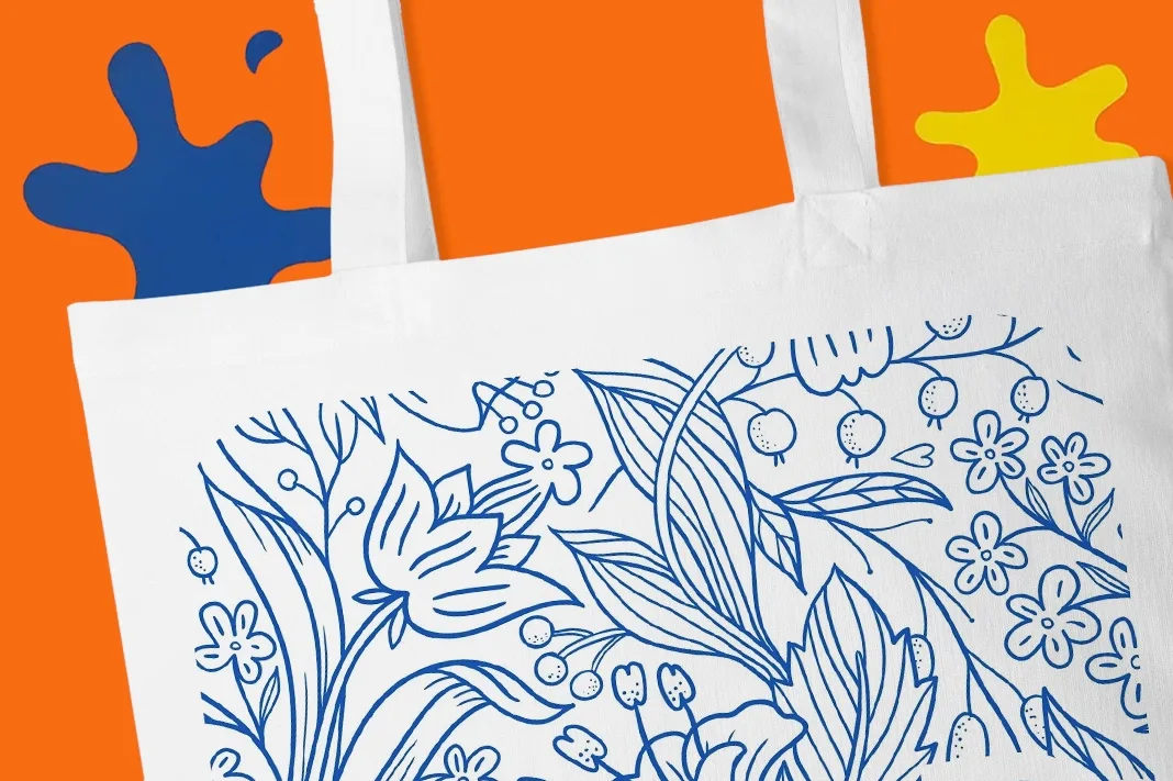 White tote bag with blue floral design on orange background, blue and yellow ink splat shapes partially visible.