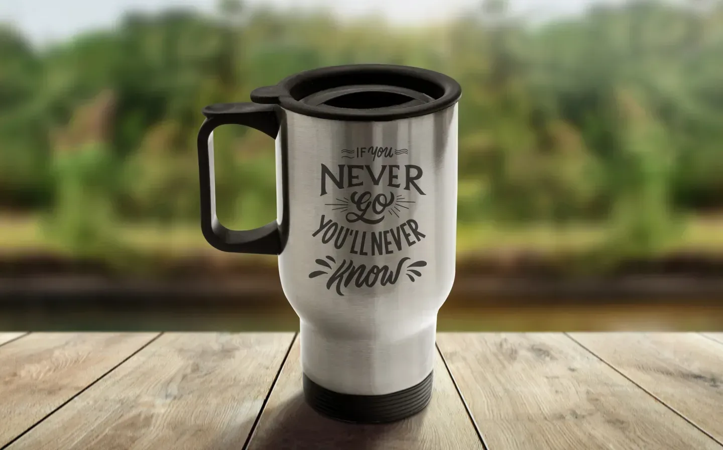 A travel mug featuring the phrase "If You Never Go, You'll Never Know", displayed on a wooden table with an outdoors backdrop