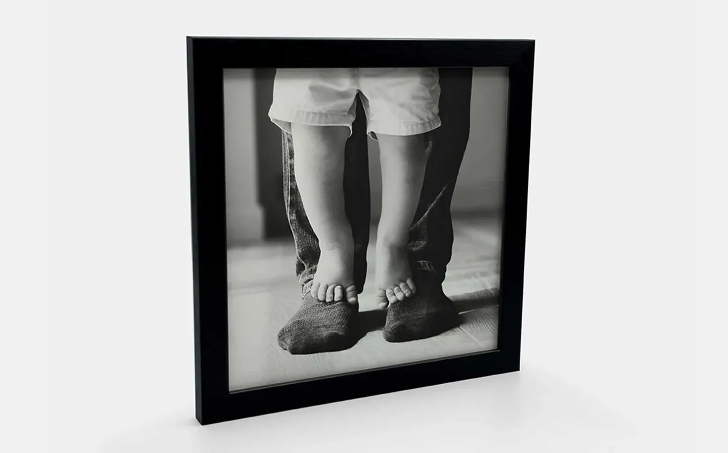 A close-up of a framed photo tile showcasing black and white photo of parent-and-child feet