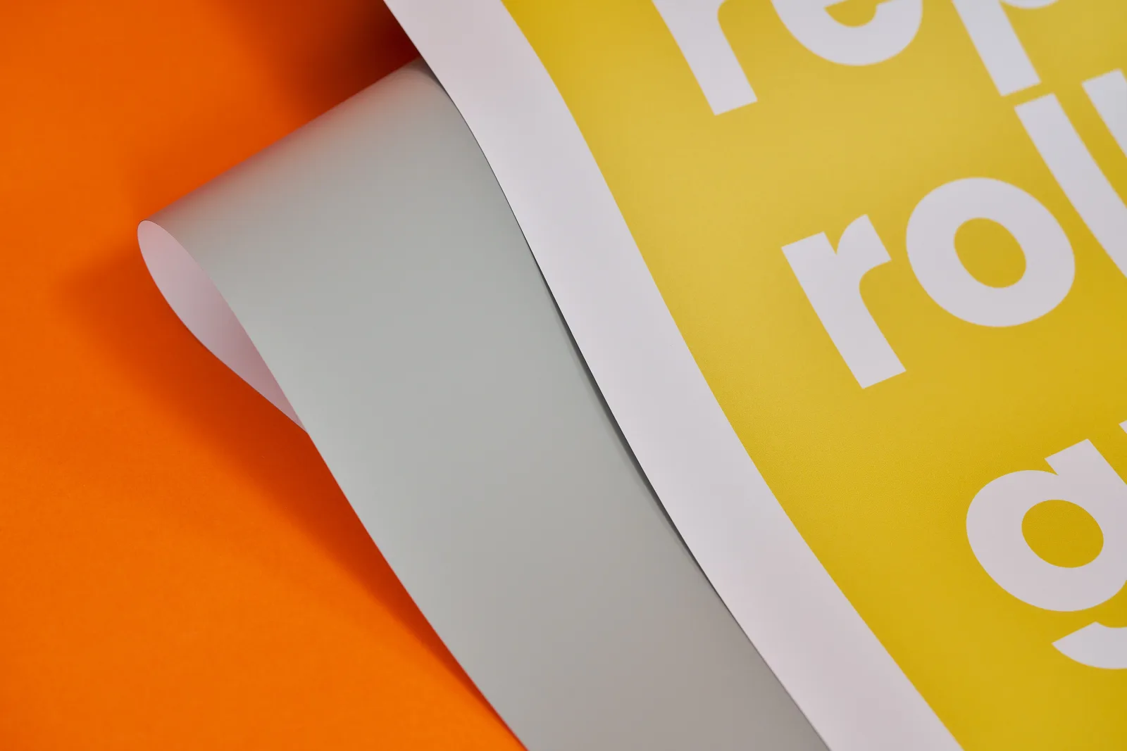 close up of a printed replacement roller banner graphic showing yellow print and the greyback PVC on a bright orange background