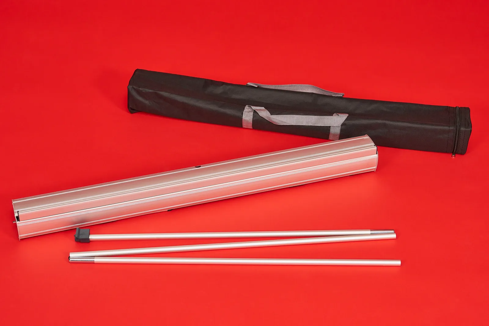 budget roller banner contents showing carry bag, silver cassette and silver support pole on a bright red background