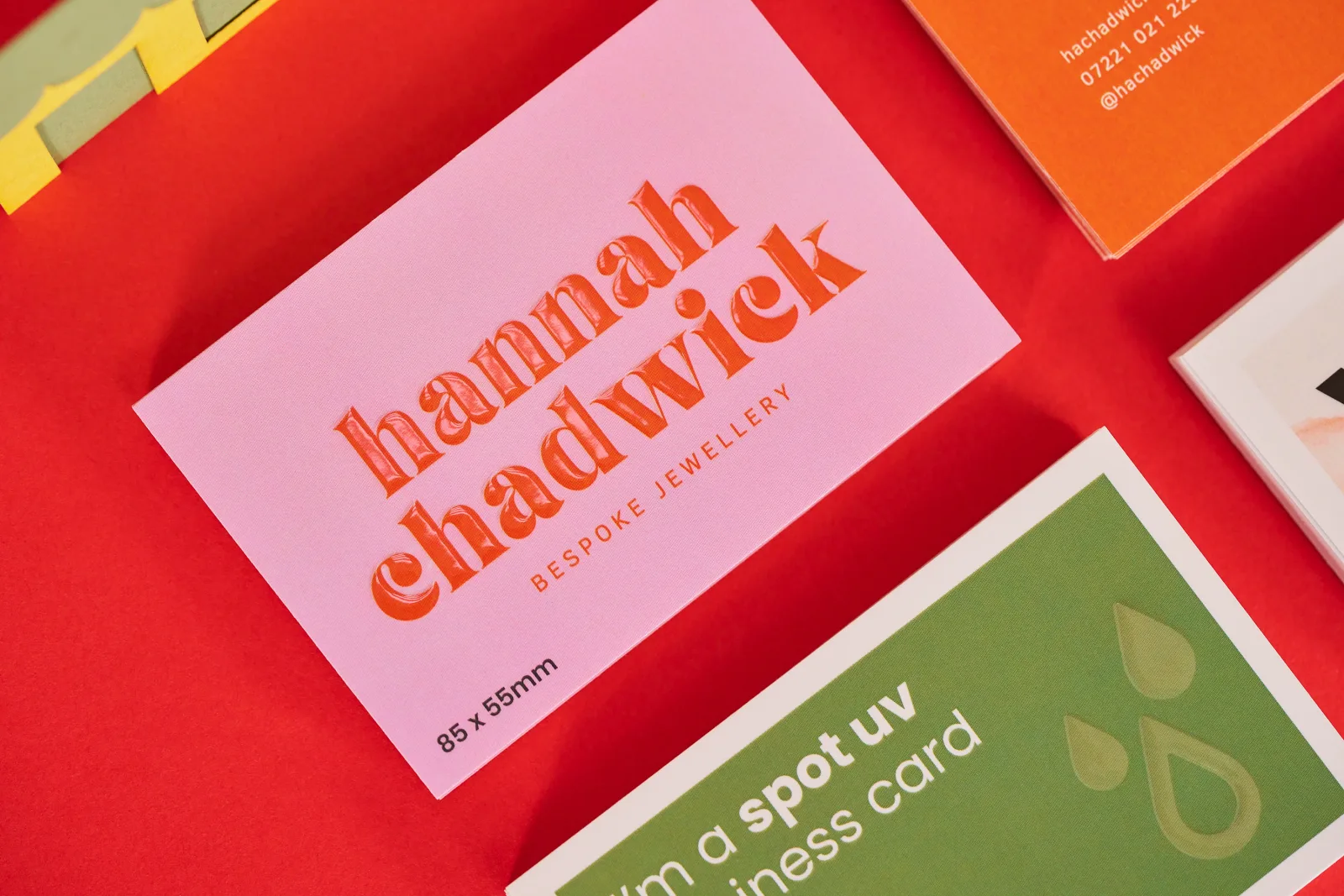 stack of pink business cards with red text 'hannah chadwick' with spot uv over the top. Green business card with text 'a spot uv card' on a bright red background