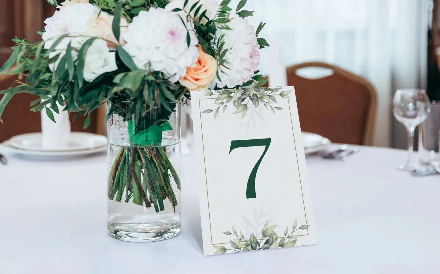 A wedding table number card displaying "7" elegantly placed next to a vase adorned with colourful flowers