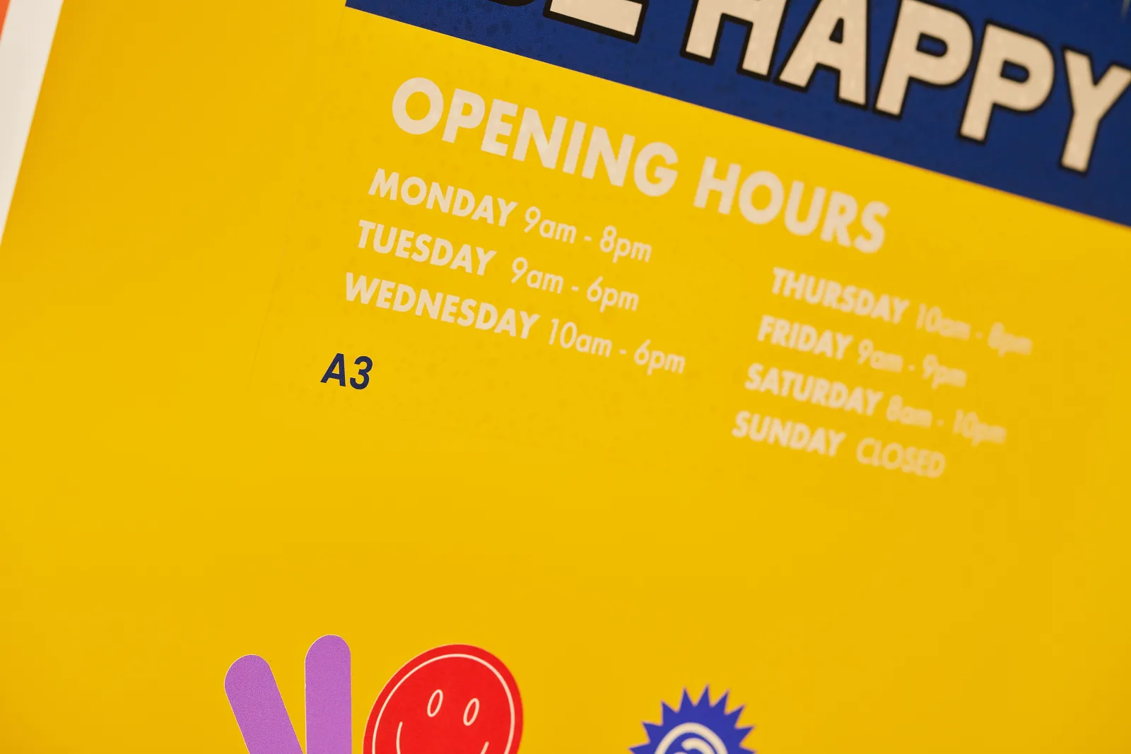 close up of a clear reverse printed vinyl window sticker with white selective ink with text 'opening hours, happy, a3' on a bright yellow background