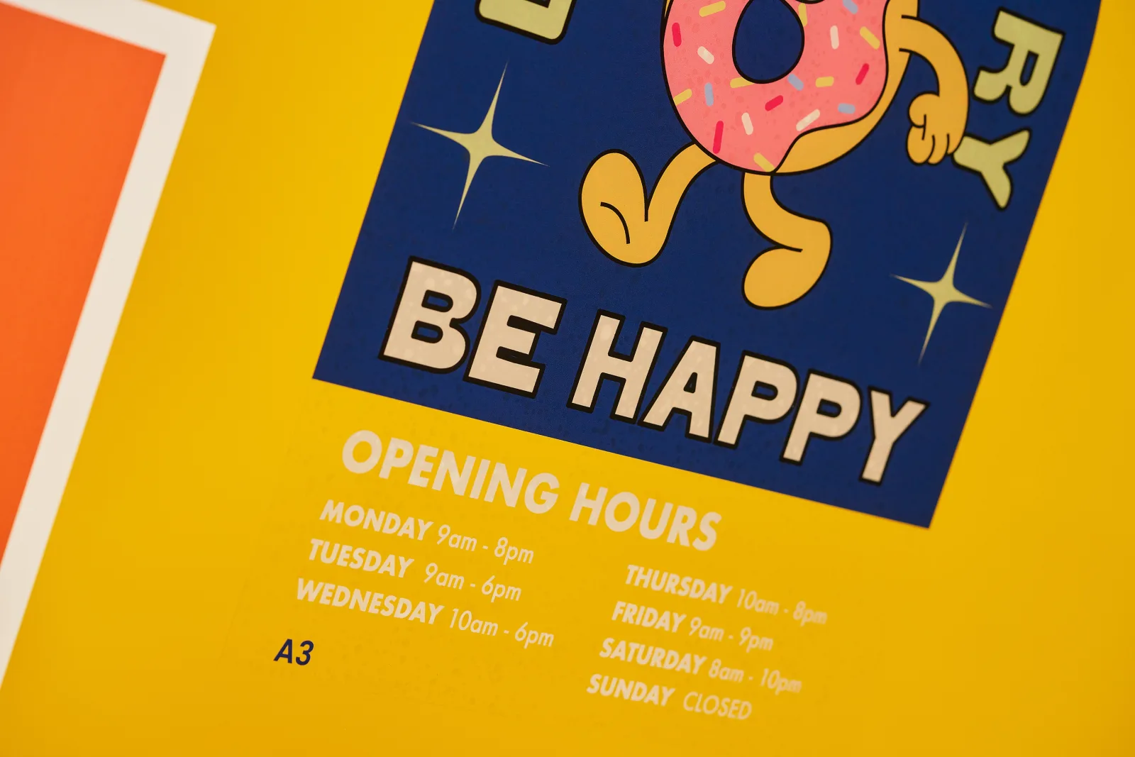 clear reverse vinyl window sticker printed in blue with a doughnut character illustration with text 'be happy, opening times, a3' on a bright yellow background