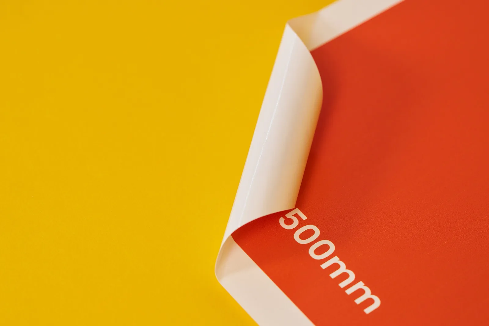 white vinyl window sticker forward printed in orange with corner curled over and text '500mm' on a bright yellow background