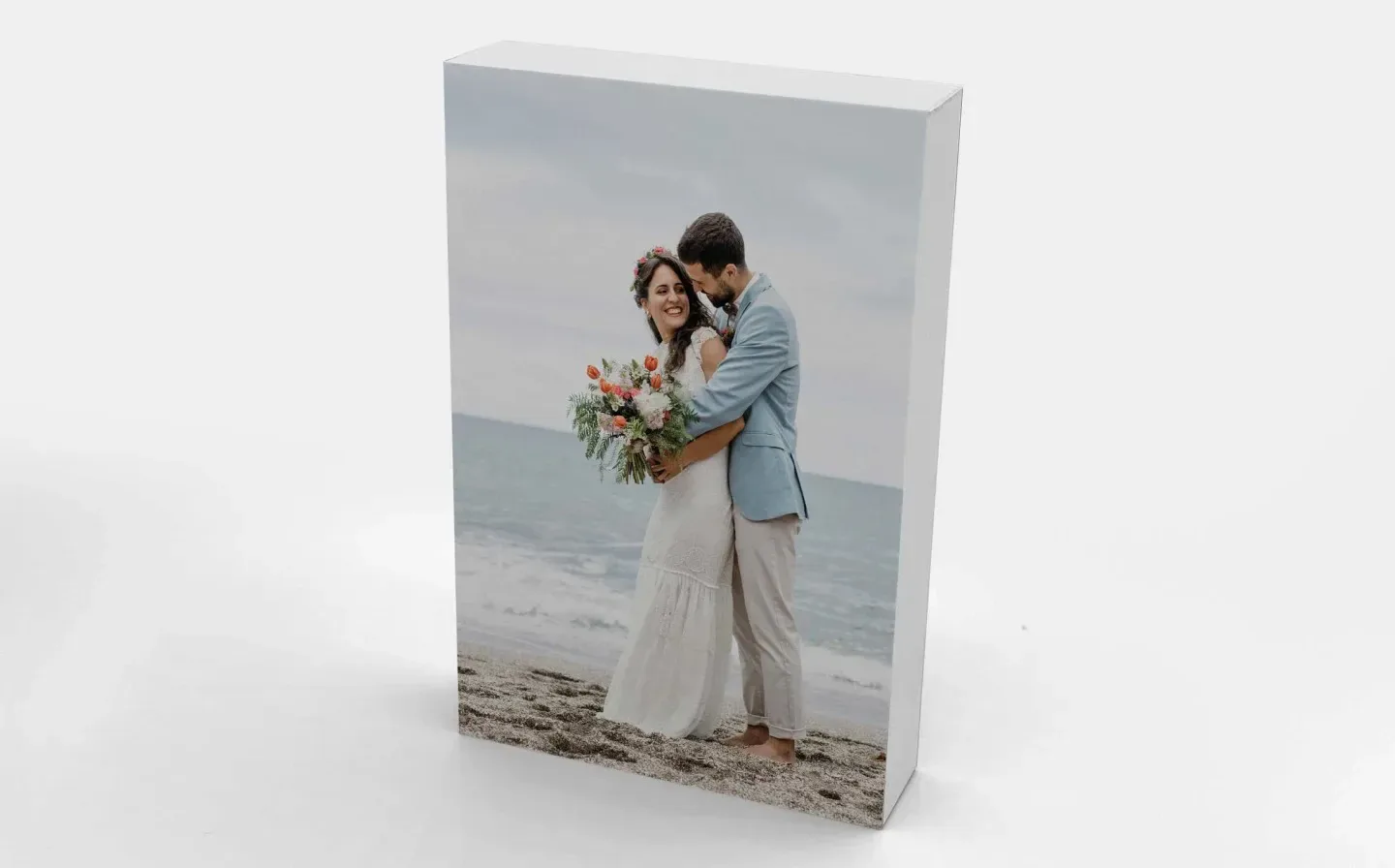A couple embraces on the beach, captured in a wedding photo displayed on a wooden block